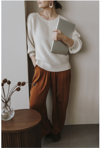 Career woman in white sweater and brown pants holding a laptop