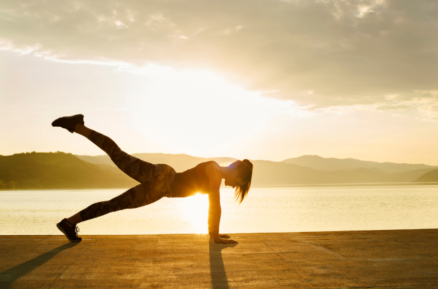 Woman making working out fun by going outside by water and doing a push-ups.