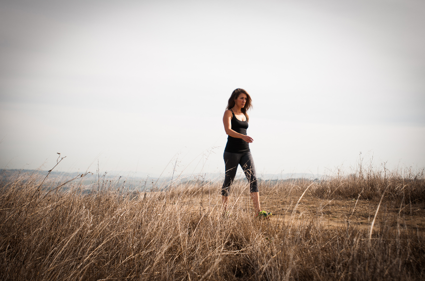 A woman in fitness attire is walking outside in nature.