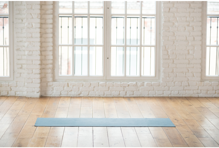 A yoga mat on a wood floor of a fitness studio with windows in the background.