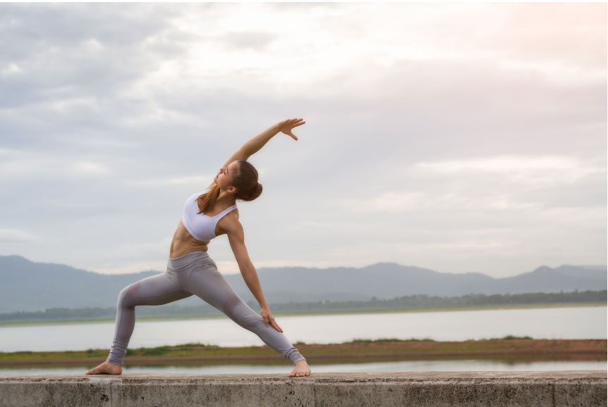 A woman is doing yoga outdoors by water.