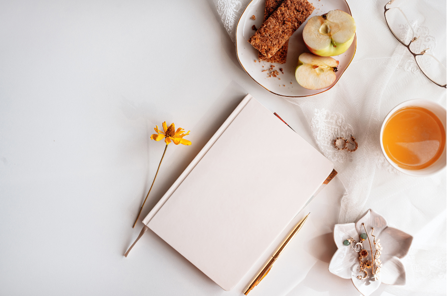 A pink journal on table with a plate of snacks.