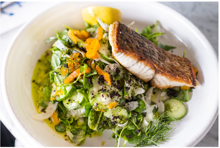 A meal showing fish with lemon and various vegetables on a white plate.