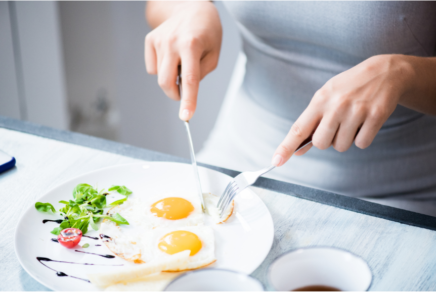 A woman eating two eggs on a plate with fork and knife.