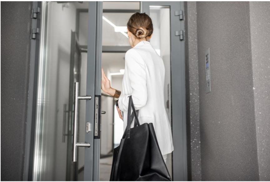 A woman in a white suit is walking through a door and leaving work.