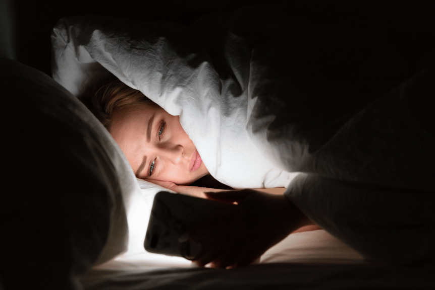 A women demonstrating unhealthy sleeping habits by scrolling on her phone in bed at night.