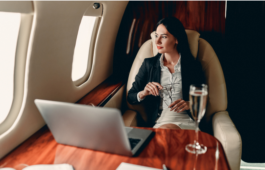 A confident successful business woman is on a first class flight with her laptop and glass of champagne.