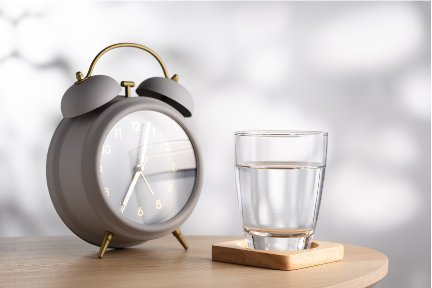 A bedside table with an alarm clock and glass of water.